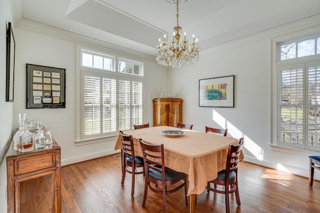 dining room featuring hardwood / wood-style flooring, ornamental molding, a raised ceiling, and a chandelier