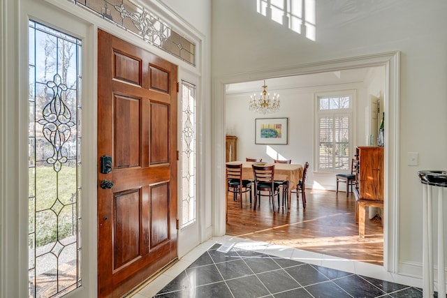 foyer entrance featuring a notable chandelier, crown molding, plenty of natural light, and dark tile patterned floors