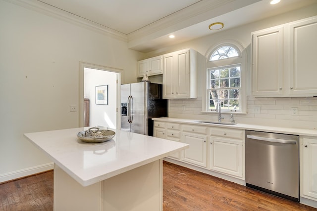 kitchen featuring a kitchen island, appliances with stainless steel finishes, sink, white cabinets, and ornamental molding