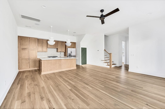 kitchen with an island with sink, stainless steel fridge, light wood-type flooring, and decorative light fixtures