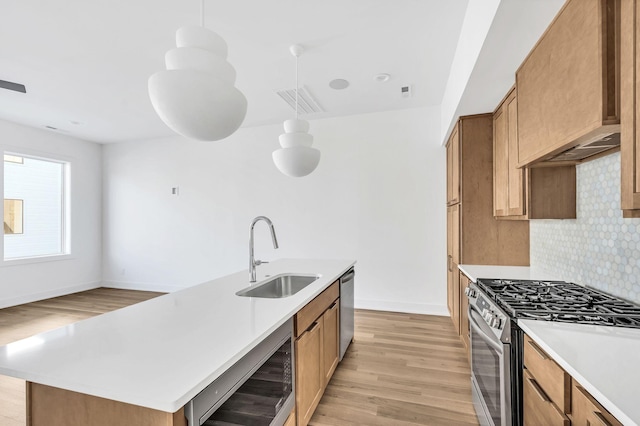 kitchen with sink, appliances with stainless steel finishes, hanging light fixtures, wine cooler, and a center island with sink