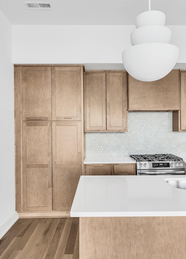 kitchen with pendant lighting, hardwood / wood-style flooring, stainless steel gas range, range hood, and decorative backsplash