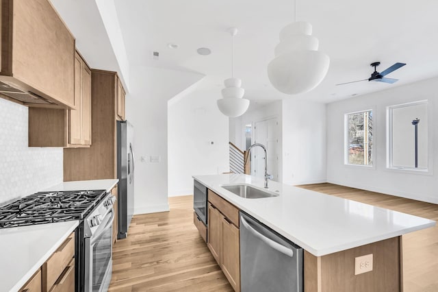 kitchen featuring pendant lighting, tasteful backsplash, sink, stainless steel appliances, and a center island with sink