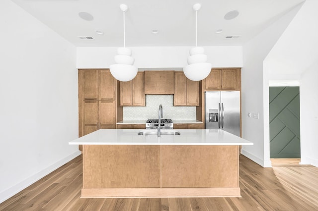 kitchen with pendant lighting, an island with sink, sink, stainless steel fridge, and decorative backsplash