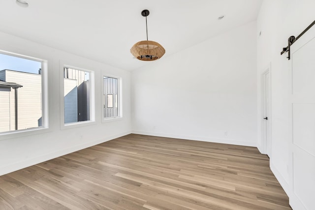 spare room featuring vaulted ceiling, a barn door, and light wood-type flooring