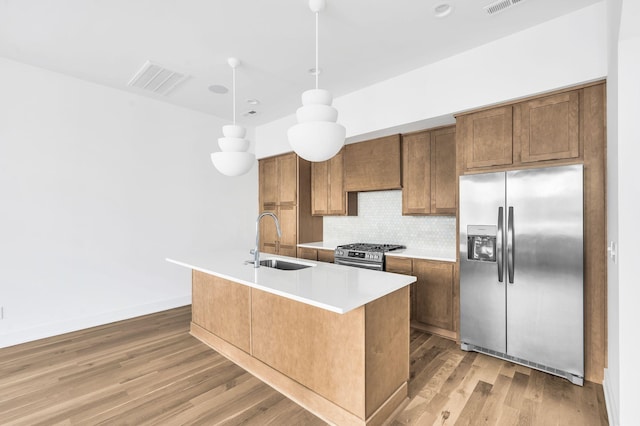 kitchen featuring appliances with stainless steel finishes, hardwood / wood-style floors, decorative light fixtures, sink, and a kitchen island with sink