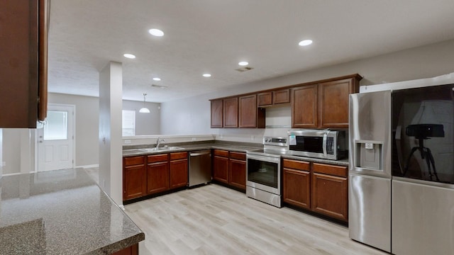 kitchen with decorative light fixtures, sink, kitchen peninsula, stainless steel appliances, and light hardwood / wood-style flooring