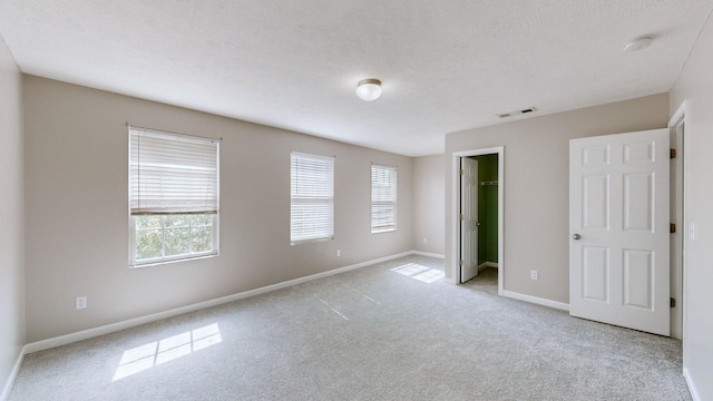 unfurnished bedroom with a spacious closet, light carpet, multiple windows, and a textured ceiling