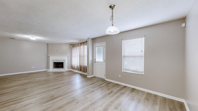 unfurnished living room featuring a fireplace, light hardwood / wood-style floors, and a textured ceiling