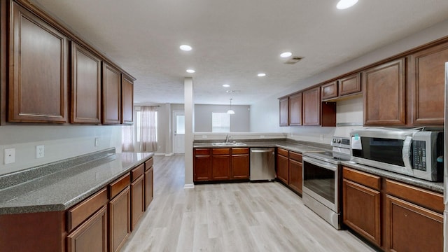 kitchen with pendant lighting, sink, light hardwood / wood-style floors, kitchen peninsula, and stainless steel appliances