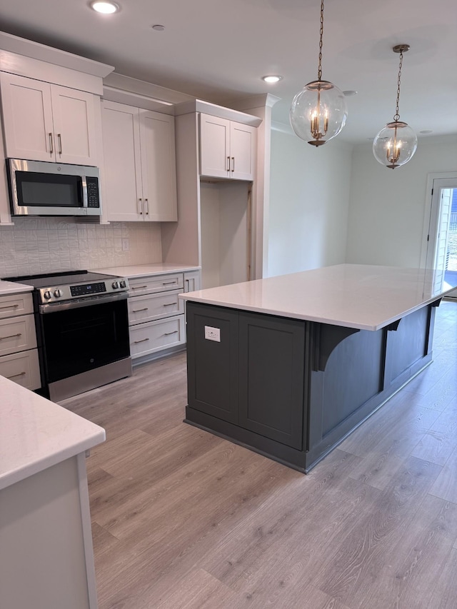 kitchen featuring decorative light fixtures, white cabinetry, a center island, stainless steel appliances, and light wood-type flooring