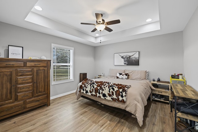 bedroom with ceiling fan, a tray ceiling, and light wood-type flooring