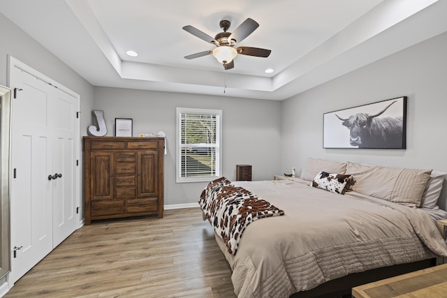 bedroom with ceiling fan, a raised ceiling, and light wood-type flooring