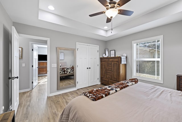 bedroom featuring a raised ceiling, ceiling fan, light wood-type flooring, and a closet