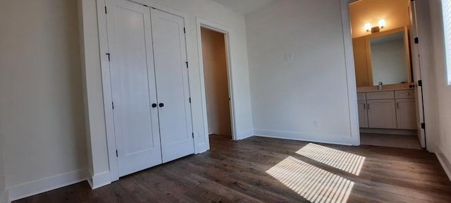 unfurnished bedroom with ensuite bathroom, dark wood-type flooring, and a closet