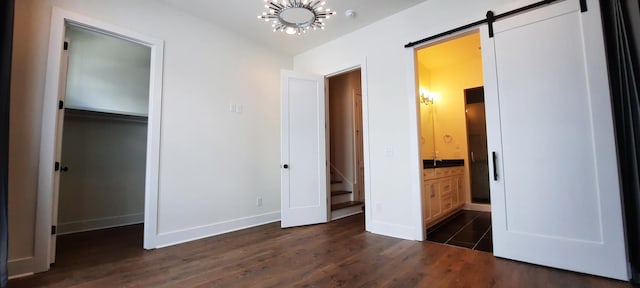 unfurnished bedroom featuring dark wood-type flooring, ensuite bath, a barn door, and a chandelier