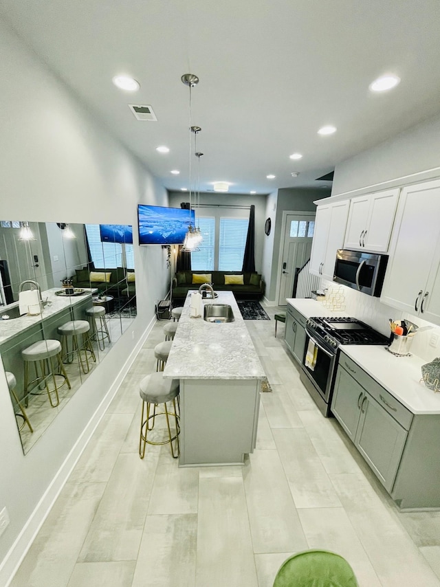 kitchen featuring pendant lighting, white cabinetry, sink, a kitchen island with sink, and gas range oven