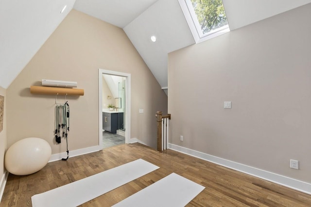 workout area with hardwood / wood-style flooring and vaulted ceiling with skylight