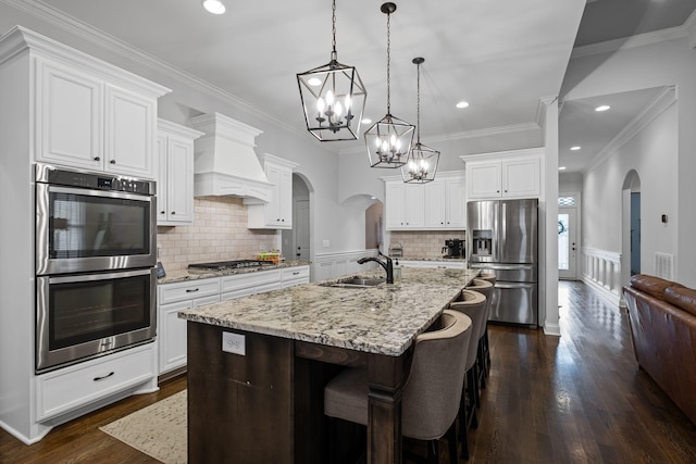 kitchen featuring stainless steel appliances, hanging light fixtures, a kitchen island with sink, and white cabinets