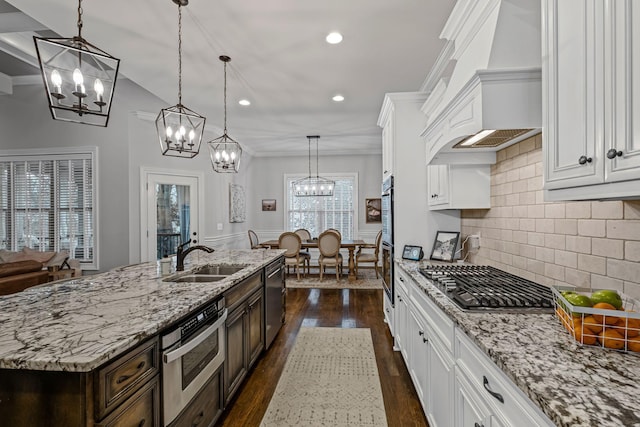 kitchen with sink, decorative light fixtures, appliances with stainless steel finishes, a kitchen island with sink, and white cabinets