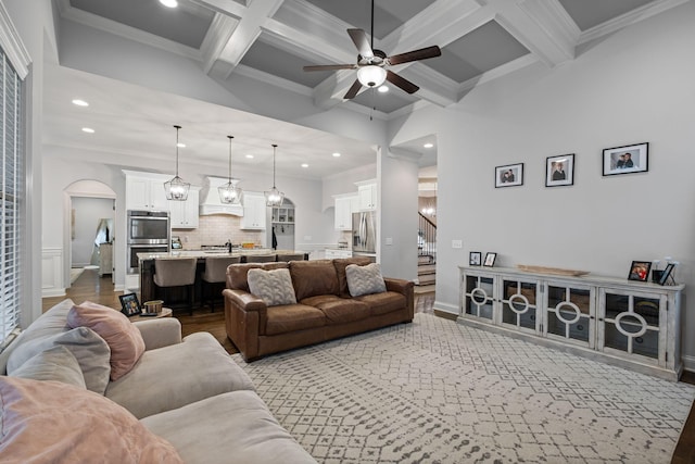 living room with beamed ceiling, ornamental molding, coffered ceiling, ceiling fan, and dark wood-type flooring