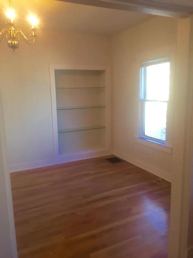 spare room featuring dark wood-type flooring and a chandelier