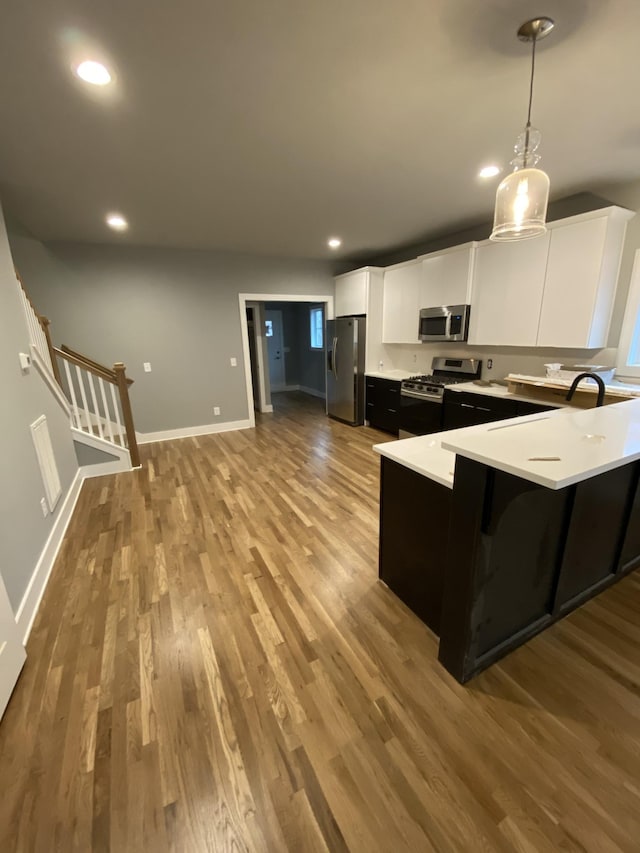 kitchen with appliances with stainless steel finishes, decorative light fixtures, white cabinetry, a breakfast bar area, and light hardwood / wood-style floors