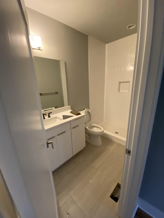 bathroom featuring wood-type flooring, walk in shower, vanity, and toilet