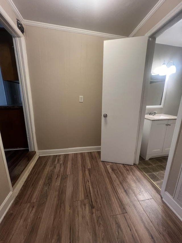 unfurnished bedroom featuring connected bathroom, sink, crown molding, and dark wood-type flooring