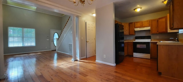 kitchen featuring white electric range oven, sink, black fridge, an inviting chandelier, and light hardwood / wood-style flooring