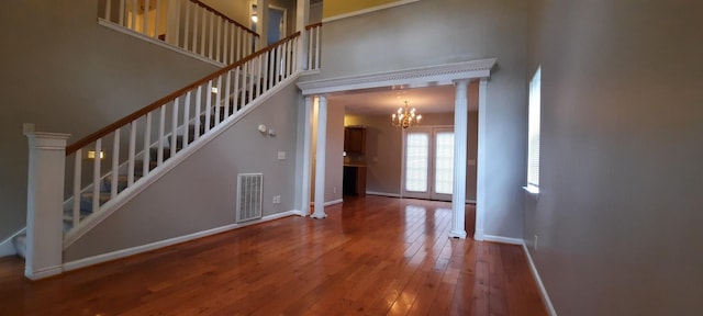 interior space featuring ornate columns, wood-type flooring, a chandelier, and a high ceiling