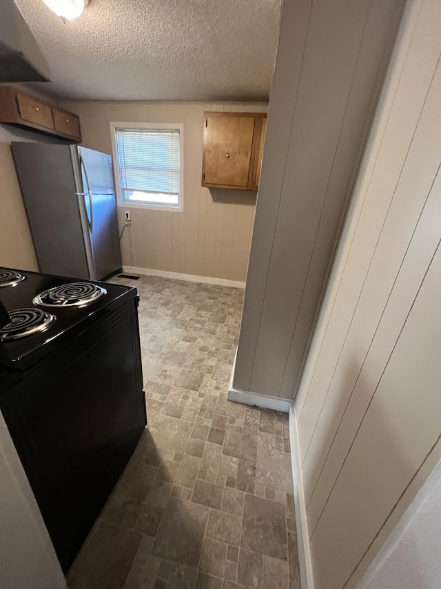 kitchen with black electric range oven, wooden walls, stainless steel refrigerator, and a textured ceiling