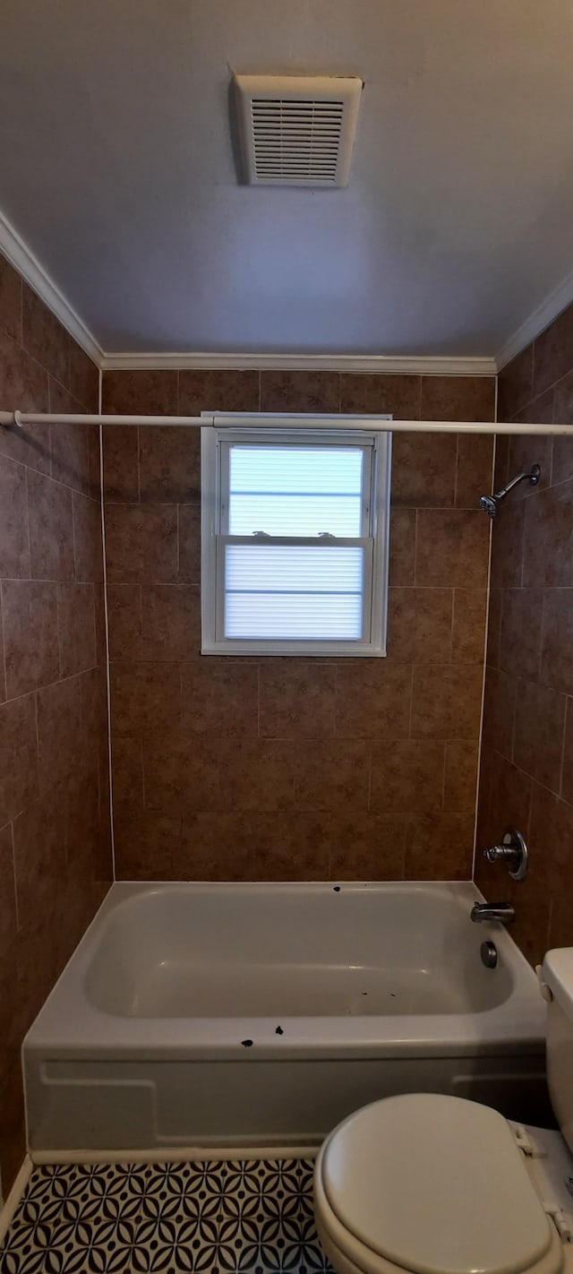 bathroom with tile patterned flooring, tiled shower / bath, crown molding, and toilet