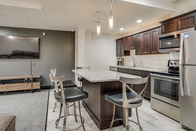 kitchen featuring a breakfast bar, stainless steel appliances, decorative backsplash, dark brown cabinetry, and light stone countertops