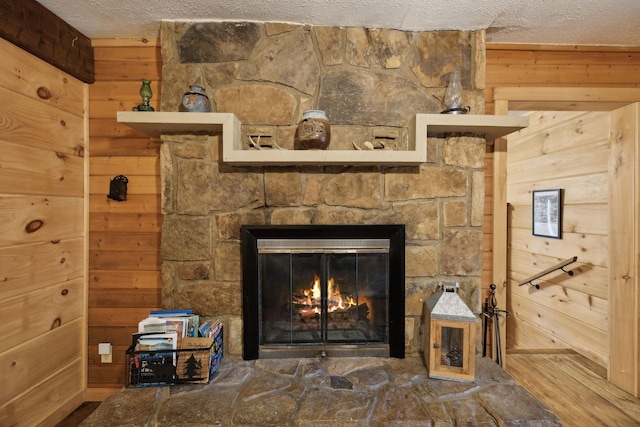 interior details featuring hardwood / wood-style flooring, a stone fireplace, a textured ceiling, and wood walls