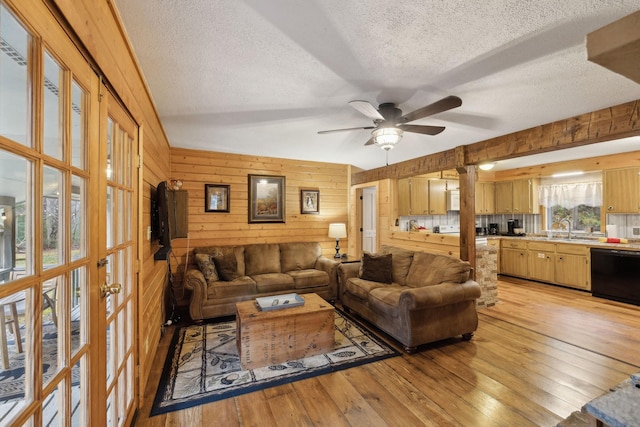 living room featuring wooden walls, sink, ceiling fan, light hardwood / wood-style floors, and a textured ceiling