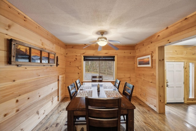 dining room with ceiling fan, wooden walls, light hardwood / wood-style flooring, and a textured ceiling