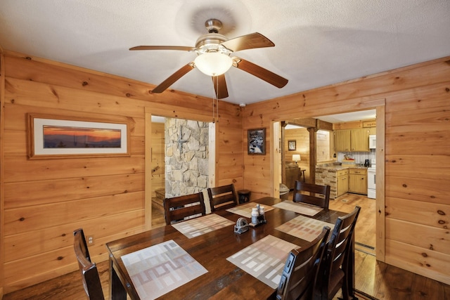 dining area with ceiling fan, light hardwood / wood-style flooring, a textured ceiling, and wood walls