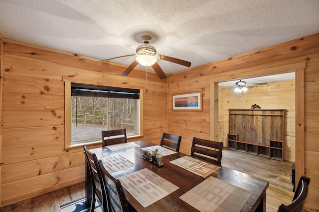 dining room with ceiling fan, wood-type flooring, a textured ceiling, and wood walls