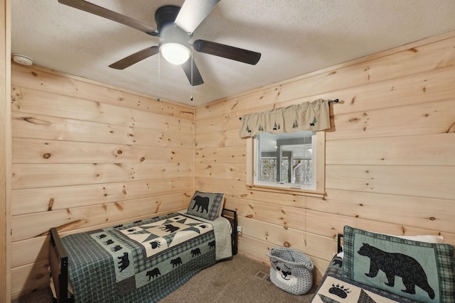 carpeted bedroom with ceiling fan, a textured ceiling, and wood walls