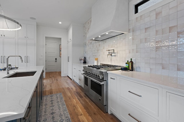 kitchen with sink, white cabinetry, light stone counters, custom range hood, and range with two ovens