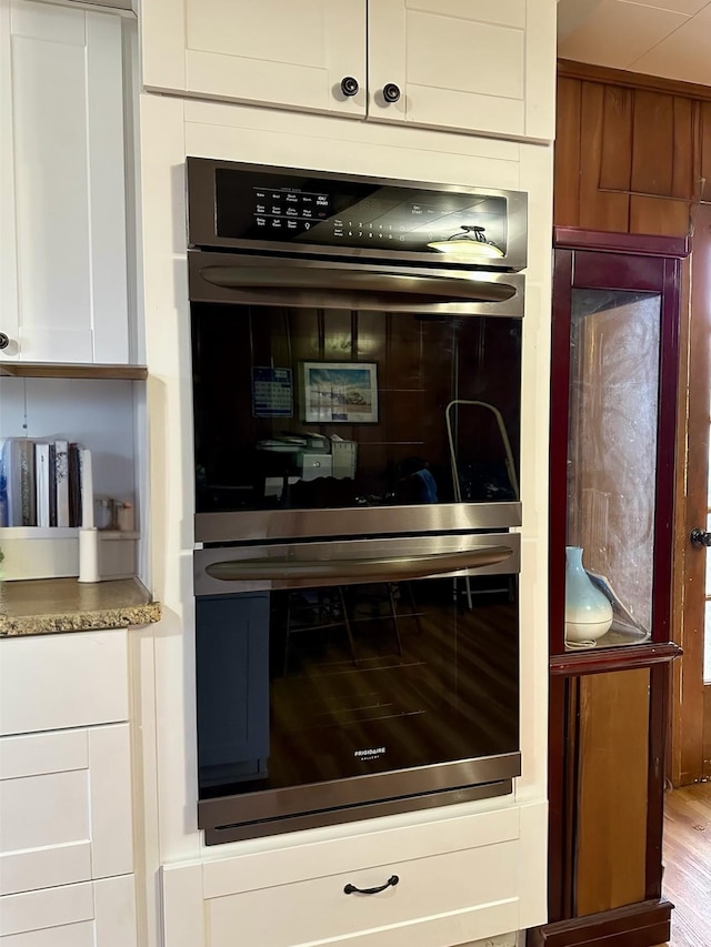 kitchen with white cabinetry, double oven, light hardwood / wood-style flooring, and stone countertops