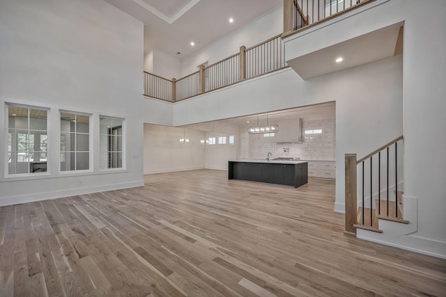 unfurnished living room featuring a high ceiling, an inviting chandelier, and light hardwood / wood-style flooring