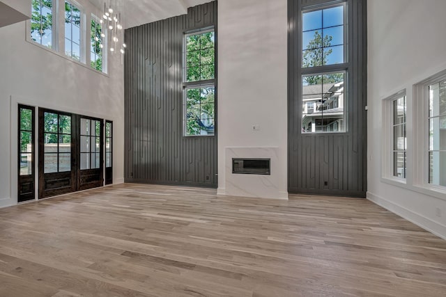 unfurnished living room with a towering ceiling, a wealth of natural light, a high end fireplace, and light hardwood / wood-style floors