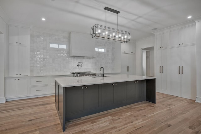 kitchen featuring pendant lighting, tasteful backsplash, white cabinetry, crown molding, and a center island with sink