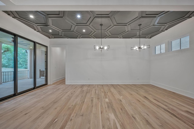 empty room featuring plenty of natural light, coffered ceiling, a chandelier, and light hardwood / wood-style flooring