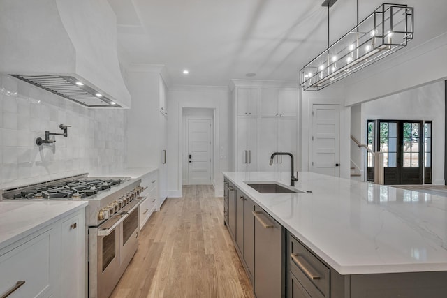 kitchen featuring pendant lighting, sink, premium range hood, white cabinetry, and appliances with stainless steel finishes