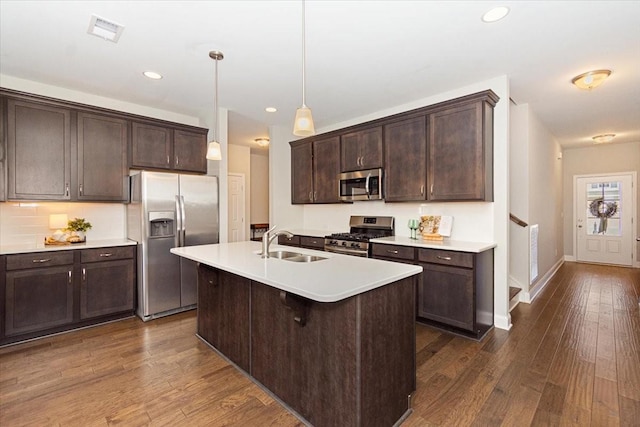 kitchen with sink, hanging light fixtures, dark hardwood / wood-style flooring, stainless steel appliances, and a kitchen island with sink