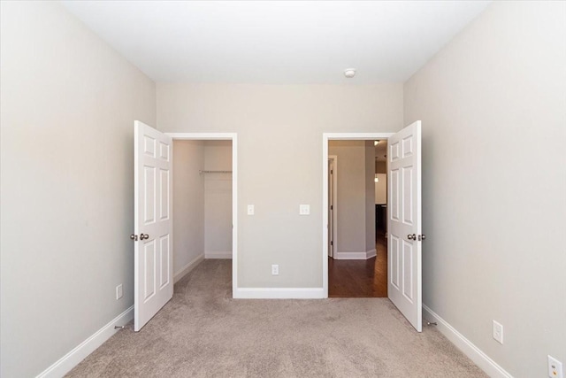 unfurnished bedroom featuring light carpet and a walk in closet