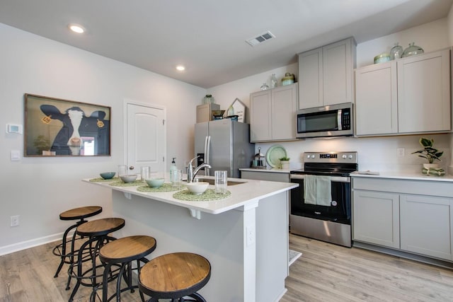 kitchen with gray cabinets, appliances with stainless steel finishes, sink, a kitchen bar, and light hardwood / wood-style flooring